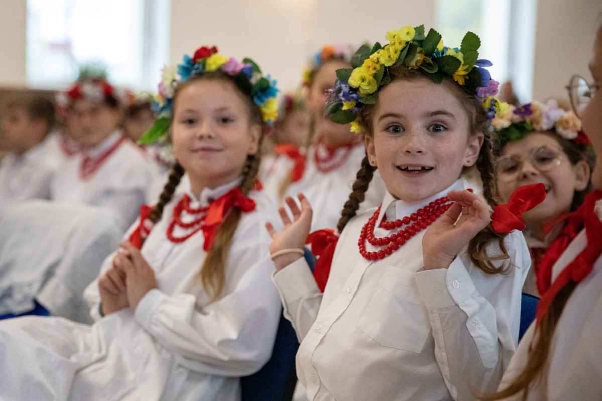 Dziewczynki w kwiecistych wiankach i czerwonych koralach pozują z uśmiechem do obiektywu.