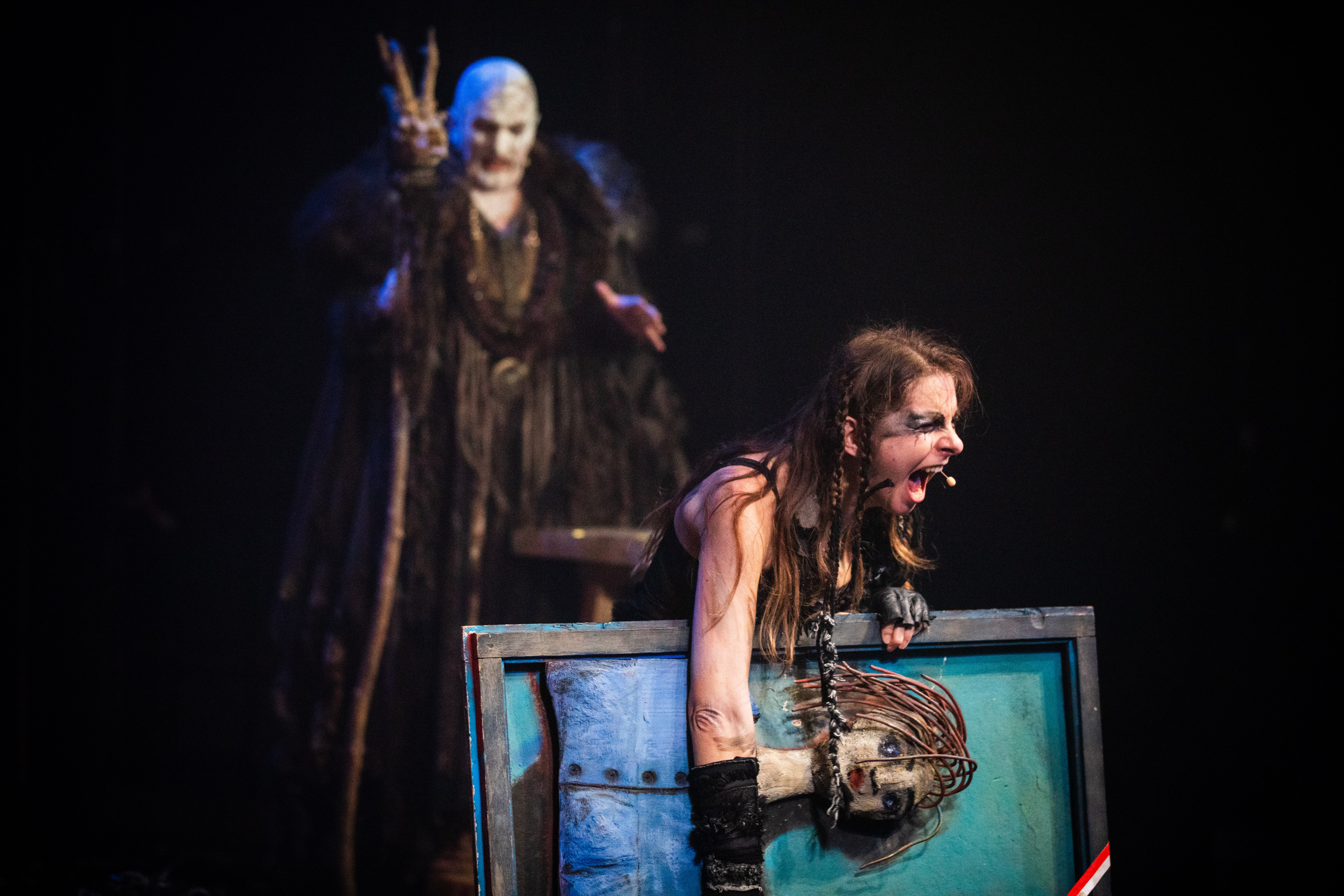 2 aktorów na scenie, z przodu młoda kobieta trzyma pod pachą duży obraz i krzyczy, w tle stoi starszy mężczyzna z twarzą pomalowaną na biało